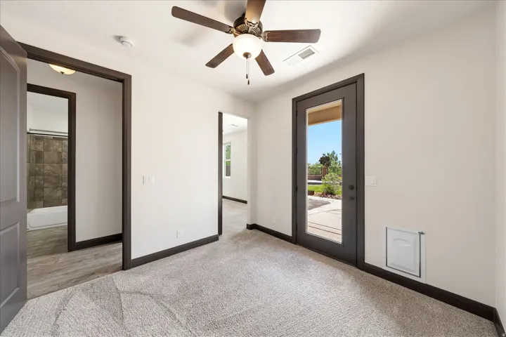 Carpeted room featuring a ceiling fan with integrated lighting, a glass-paneled door leading to an outdoor patio, and dark trim