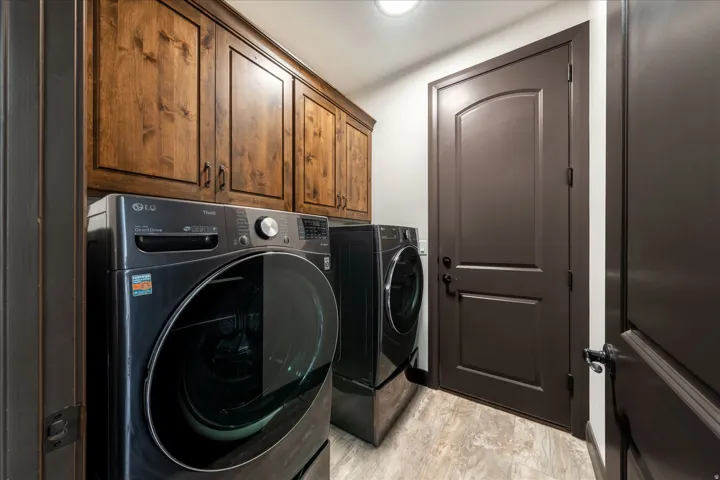 Laundry area featuring rich wood cabinetry, light-toned wood-finish flooring, and a dark paneled door