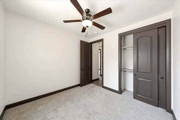 Neutral-toned bedroom featuring plush gray carpeting, a dark wood-finish ceiling fan with integrated lighting, and white walls