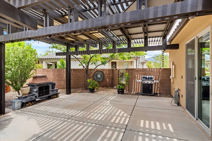 Outdoor patio featuring a dark wood-finish pergola, concrete pavers, a stone-clad outdoor fireplace, and sliding glass door access