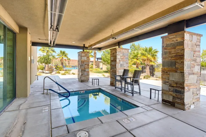 Covered patio featuring an in-ground spa with a handrail, stone-clad support columns, and an integrated ceiling heater