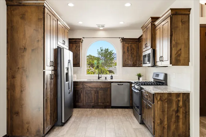 Kitchen featuring extensive wood cabinetry, light stone countertops, stainless steel appliances, a white subway tile backsplash, and wood-finish flooring