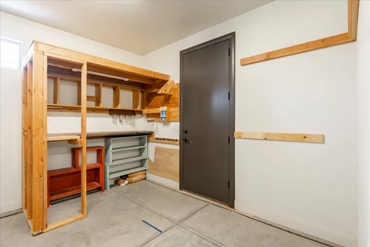 Garage workshop area featuring built-in wooden shelving, a spacious workbench, concrete flooring, and a window for natural light