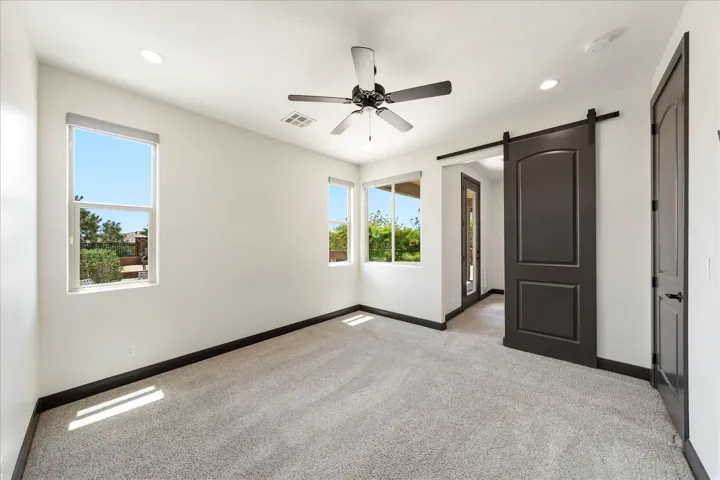 Spacious room featuring light gray carpeting, multiple windows with natural light, recessed lighting, and a dark-toned barn door