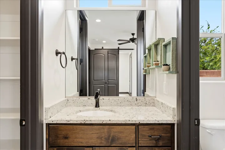 Vanity area featuring a granite-style countertop with an undermount sink, a dark wood-finish cabinet with dark hardware, and a large wall-mounted mirror