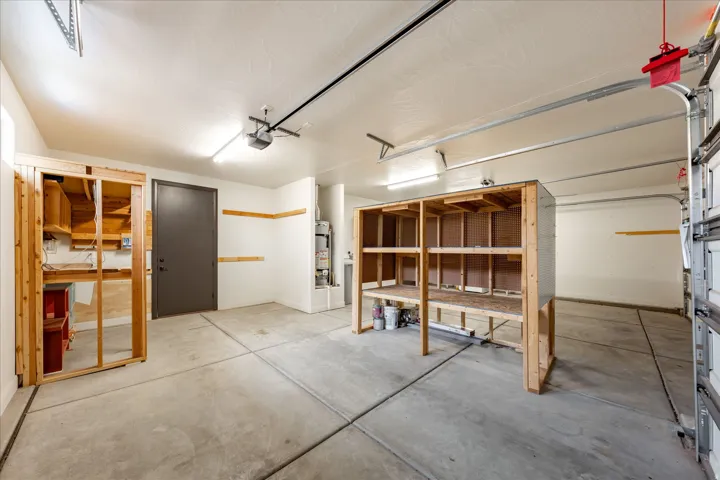 Spacious garage featuring concrete flooring, built-in wooden shelving, a dark-paneled entry door, and an automatic garage door opener