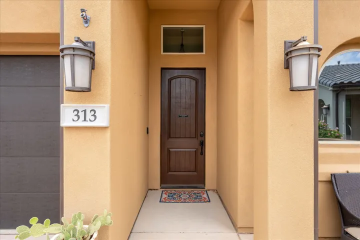 Stucco exterior with a paneled wood-finish entry door, transom window, and two exterior wall lanterns