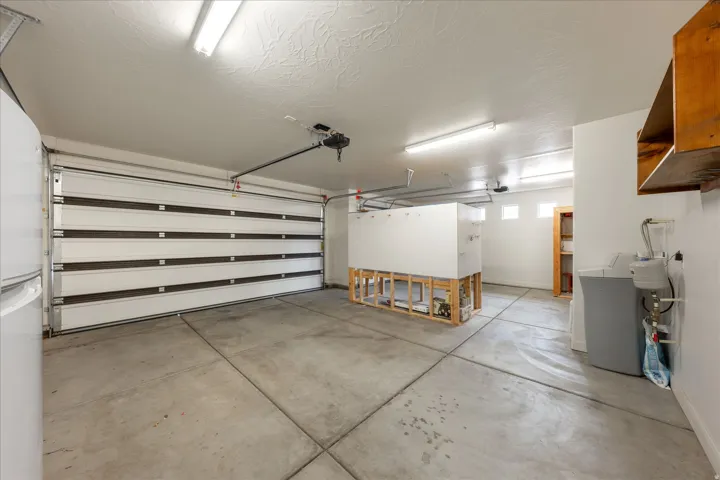Spacious garage featuring a sectional overhead door with automatic opener, concrete flooring, and multiple fluorescent light fixtures