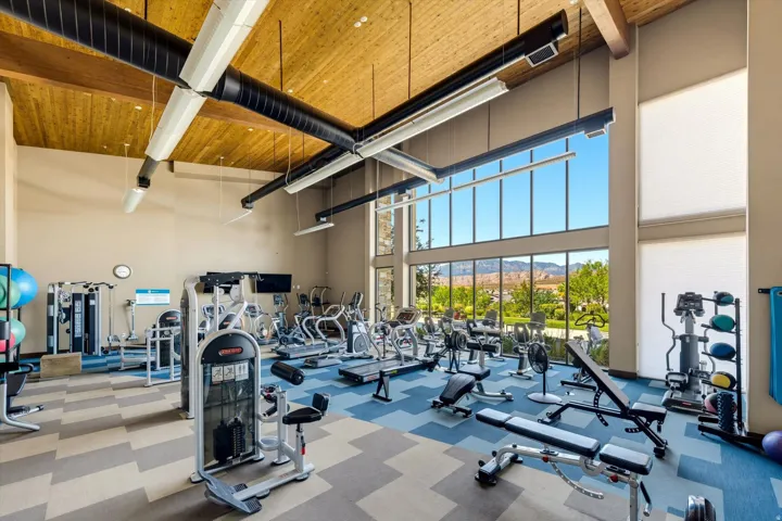 Open-concept fitness center featuring a high wood-paneled ceiling, exposed beam accents, and expansive floor-to-ceiling windows