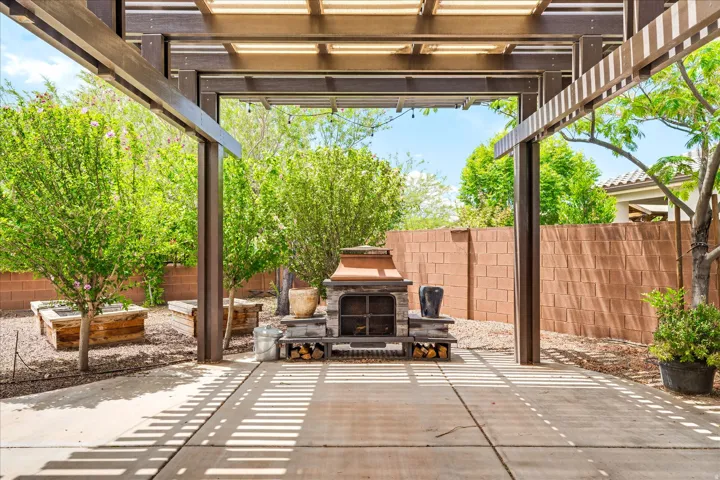 Spacious outdoor patio with a full pergola, featuring an integrated fireplace, privacy walls, and established plantings