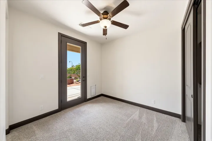 Spacious room with light-colored carpet flooring, dark wood-finish trim, a ceiling fan with integrated lighting, and a glass-paneled exterior door