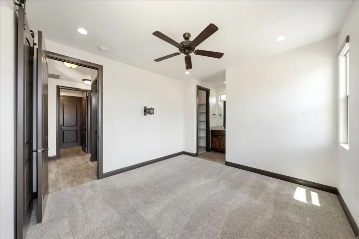 Spacious room featuring light gray carpeting, dark wood-finish trim, and a ceiling fan with integrated lighting