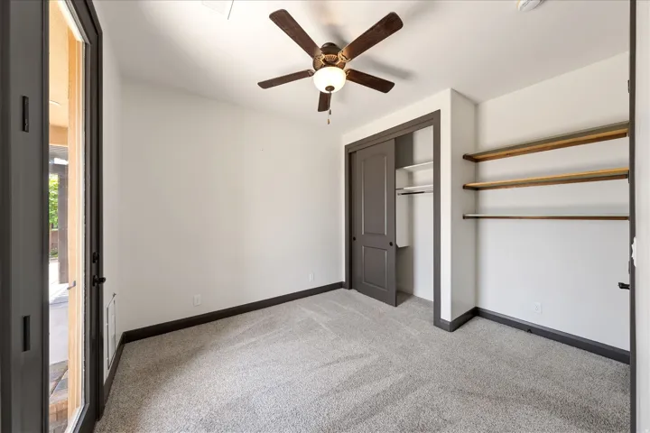 Carpeted room featuring a ceiling fan with light, a sliding closet door, built-in shelving, and direct outdoor access through a glass-paneled door