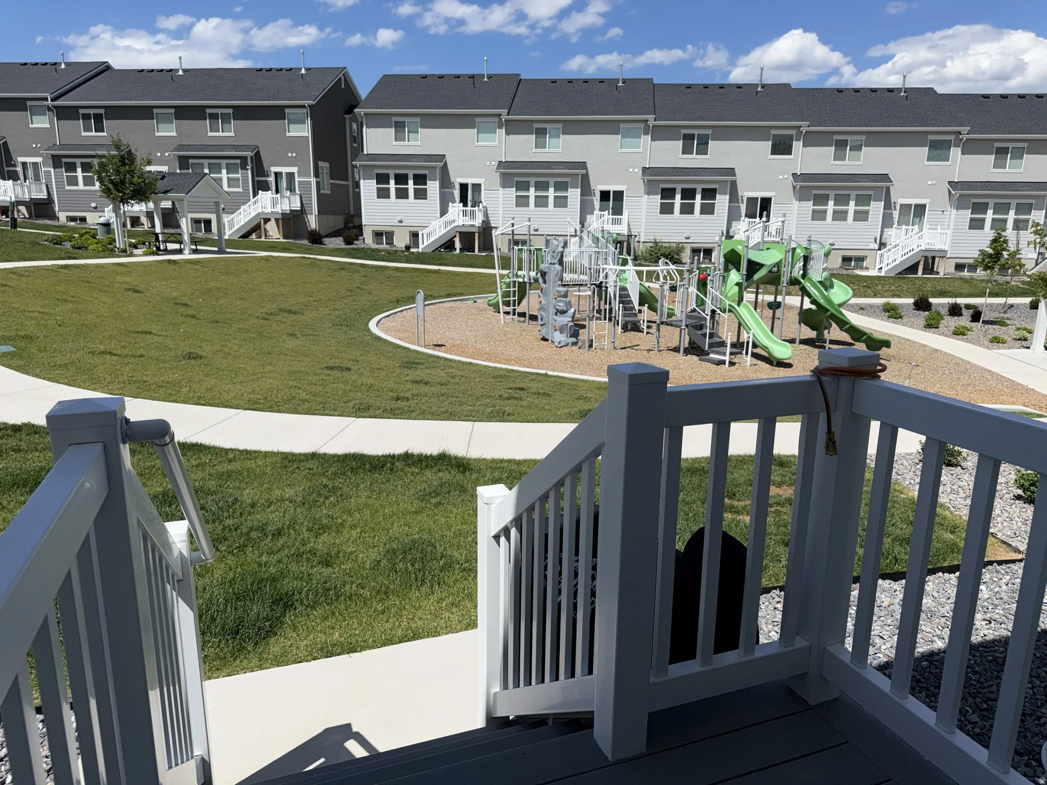 Community playground featuring a variety of recreational equipment, surrounded by manicured green spaces and paved walking paths