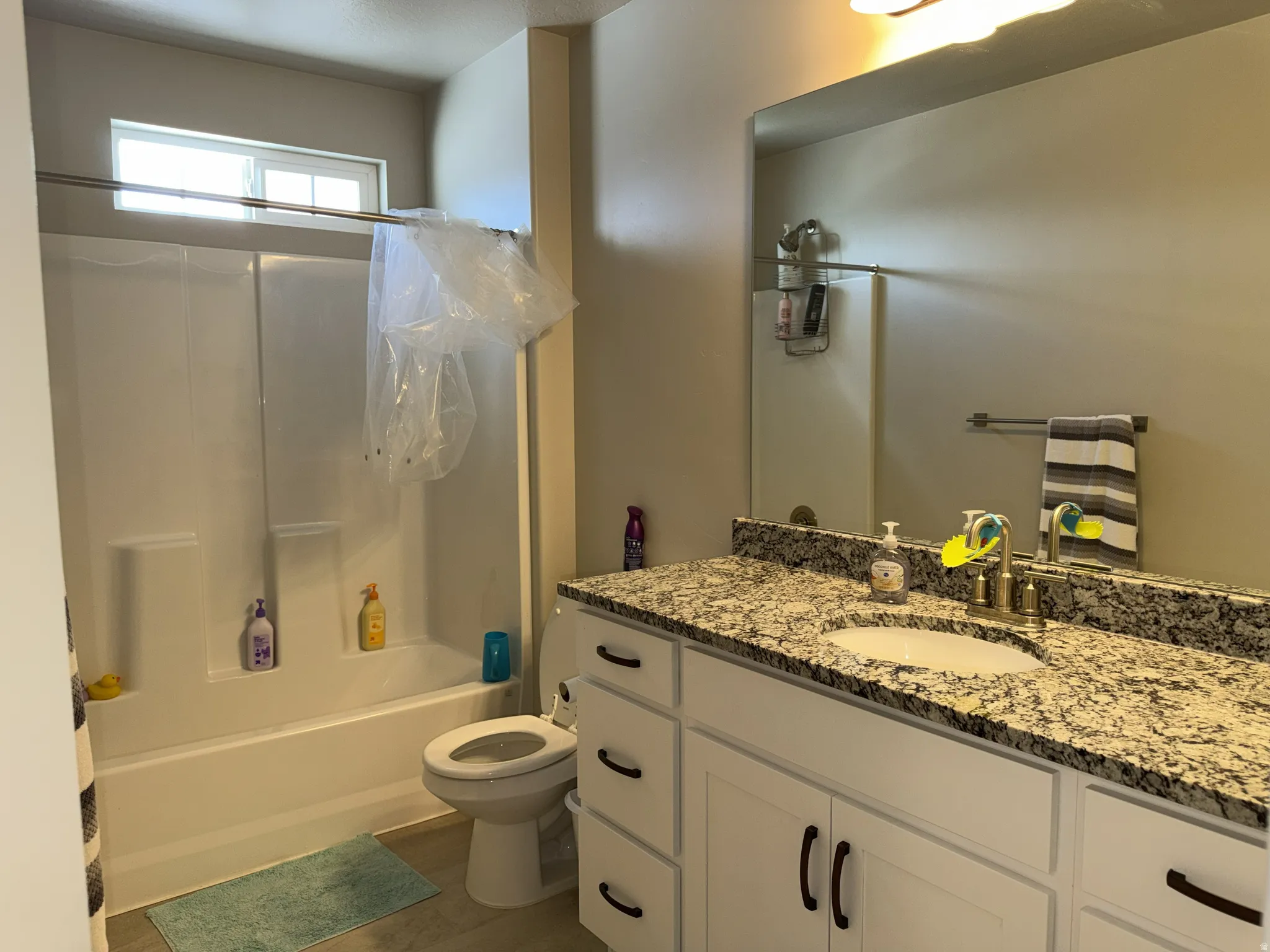 Bathroom with a white vanity featuring dark hardware, a speckled countertop, an undermount sink, and a built-in shower/tub combination