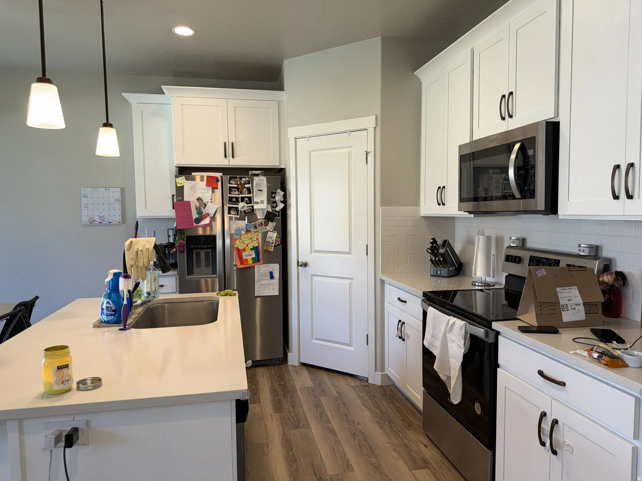 Kitchen featuring white shaker-style cabinetry, stainless steel appliances, light-toned countertops, and wood-finish flooring