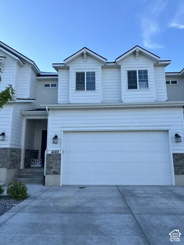 Contemporary white siding exterior featuring a two-car garage with panel detailing, stone accents, and two prominent dormer windows