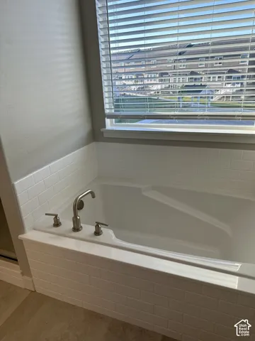 Soaking tub with white subway tile surround, brushed nickel fixtures, and light wood-finish flooring