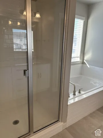 Contemporary bathroom featuring a glass-enclosed shower, a built-in bathtub with brushed nickel fixtures, a window with blinds, and light-toned flooring