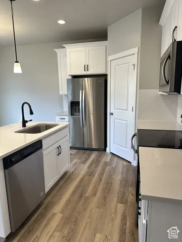 Modern kitchen featuring white shaker cabinetry, stainless steel appliances, light countertops, wood-finish flooring, and a white subway tile backsplash