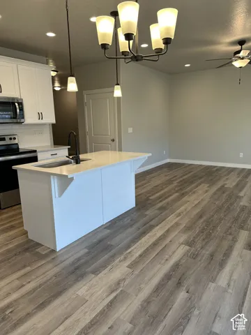 Open-concept living area with wood-finish flooring, a contemporary kitchen island with a built-in sink, stainless steel appliances, and white shaker cabinetry