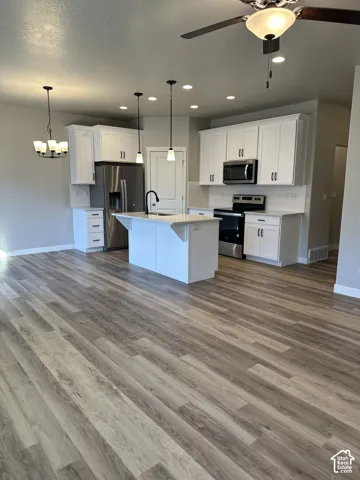 Kitchen featuring white cabinetry, stainless steel appliances, a center island with a sink, pendant lighting, and wood-finish flooring