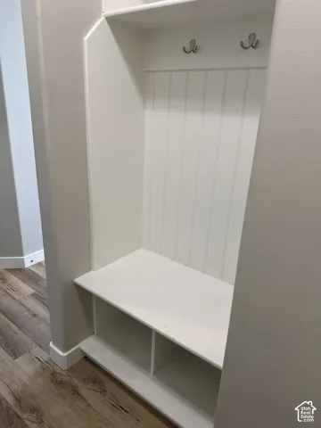 Built-in entryway bench featuring a beadboard back panel, two coat hooks, open storage compartments, and a wood-finish flooring