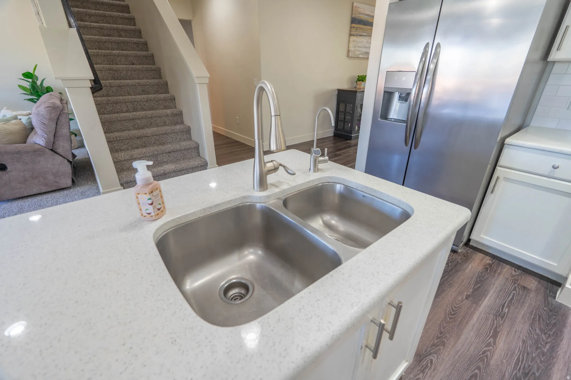 Kitchen island featuring a double basin stainless steel sink with a gooseneck faucet, white speckled countertop, and white cabinetry with silver hardware