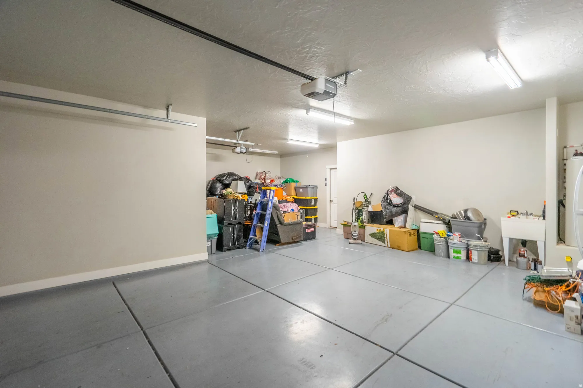 Expansive garage featuring gray finished concrete flooring, a utility sink, multiple fluorescent light fixtures, and a white interior door