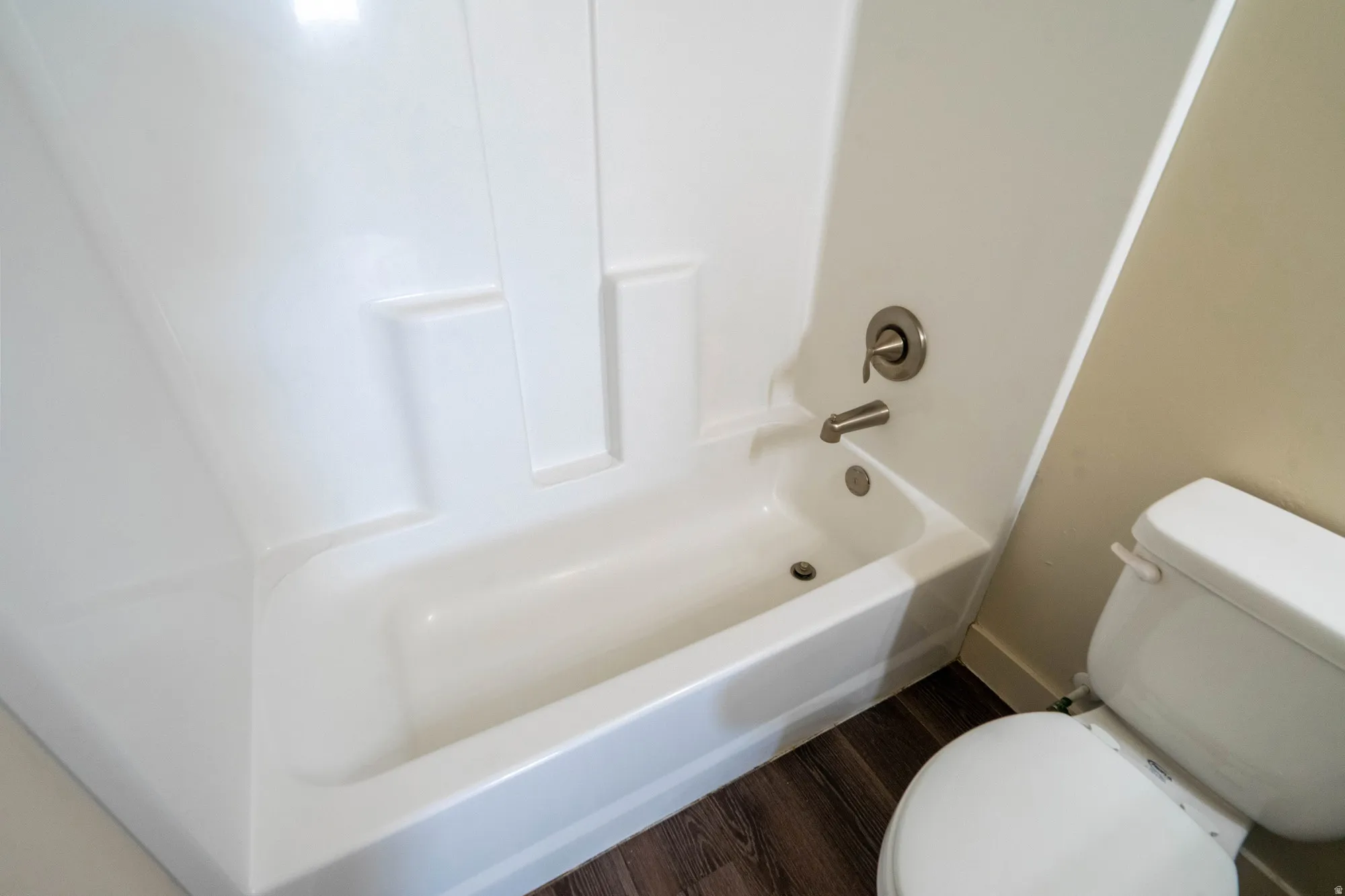 Integrated white tub and shower unit with brushed nickel fixtures, complemented by wood-finish flooring and a white toilet