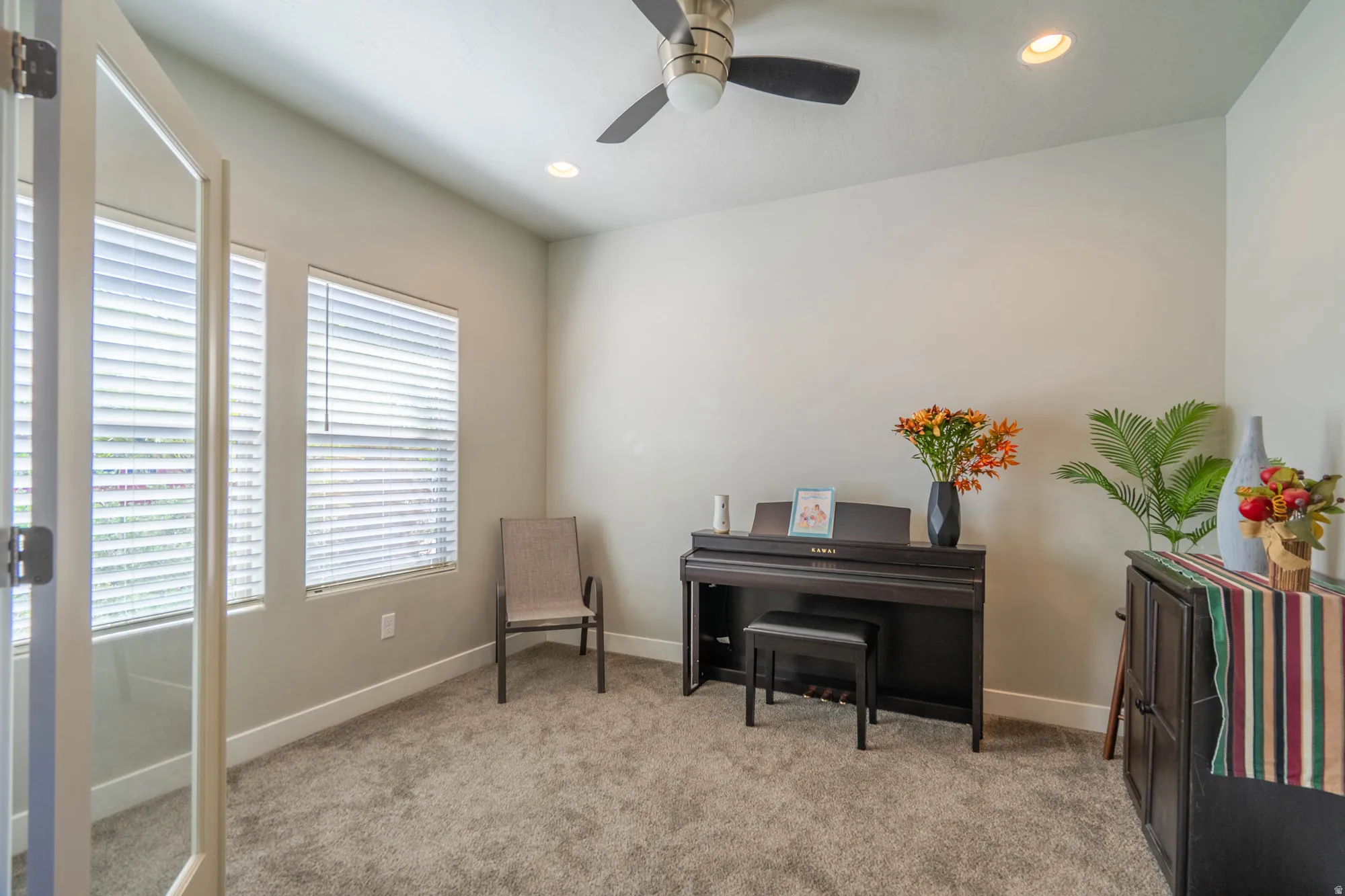 Carpeted interior room featuring a ceiling fan with integrated lighting, recessed lighting, and two windows with blinds