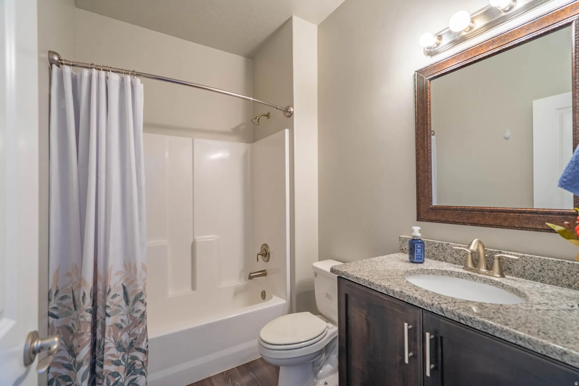 Bathroom featuring a full tub/shower combination, dark wood-finish vanity with granite-style countertop, undermount sink, and a framed mirror with vanity lighting