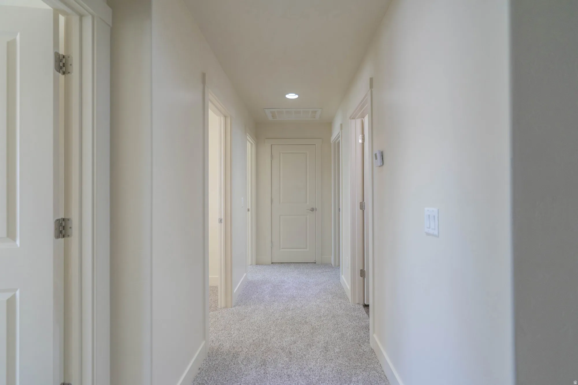 Hallway featuring light gray carpeting, white walls, recessed ceiling lighting, and multiple paneled doors