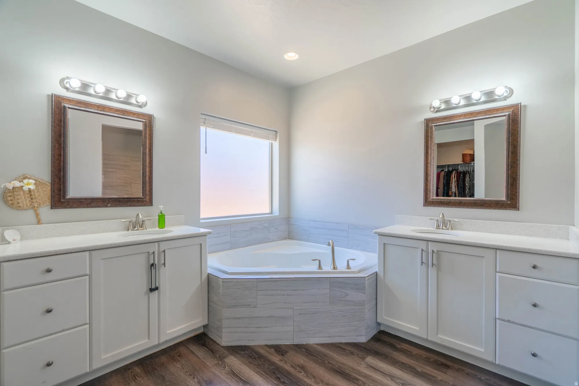 Bathroom featuring a corner soaking tub with tile surround, dual vanities with white cabinetry, integrated sinks, and individual mirrors with vanity lighting