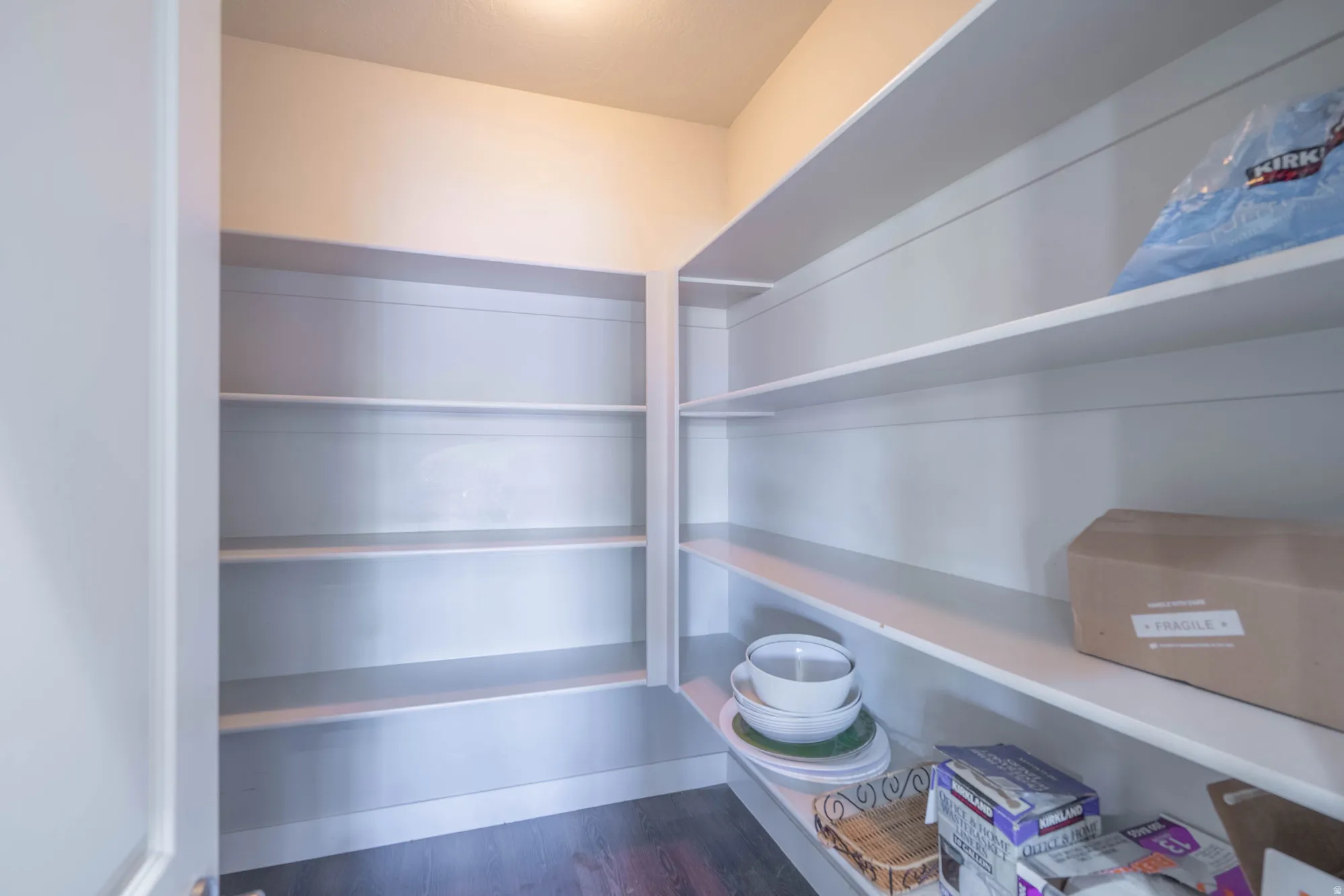 Walk-in pantry featuring extensive built-in shelving, durable wood-finish flooring, and bright overhead lighting