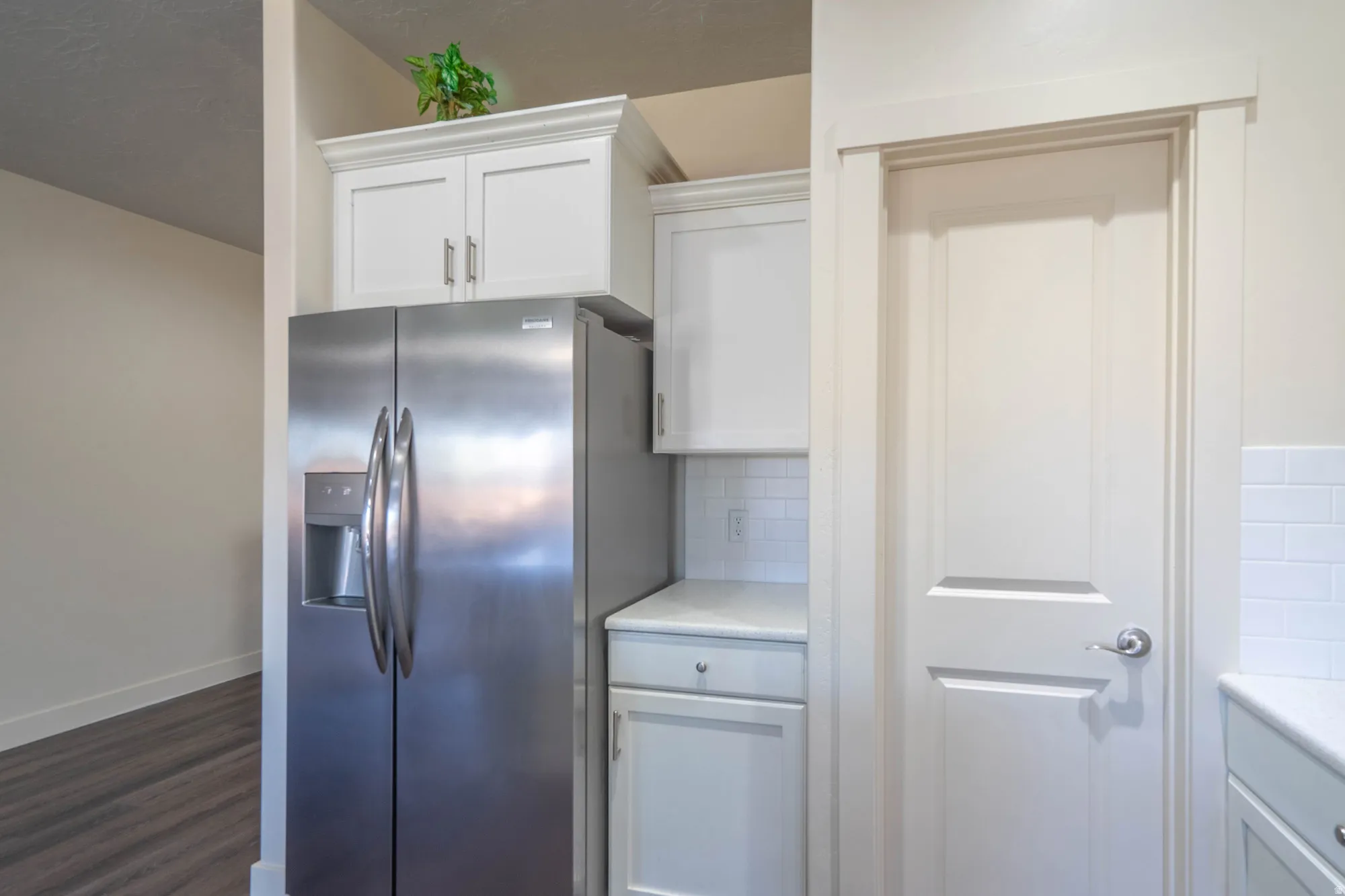Stainless steel side-by-side refrigerator, white upper and lower cabinetry, white subway tile backsplash, and light-toned countertops