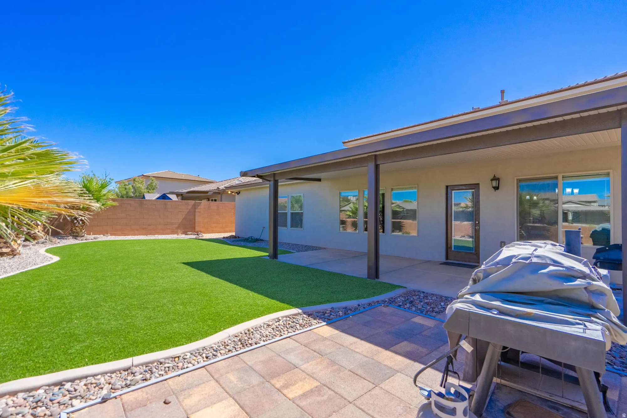 Private backyard featuring synthetic turf, decorative rock landscaping, a block wall perimeter, and a covered patio with a paver surface