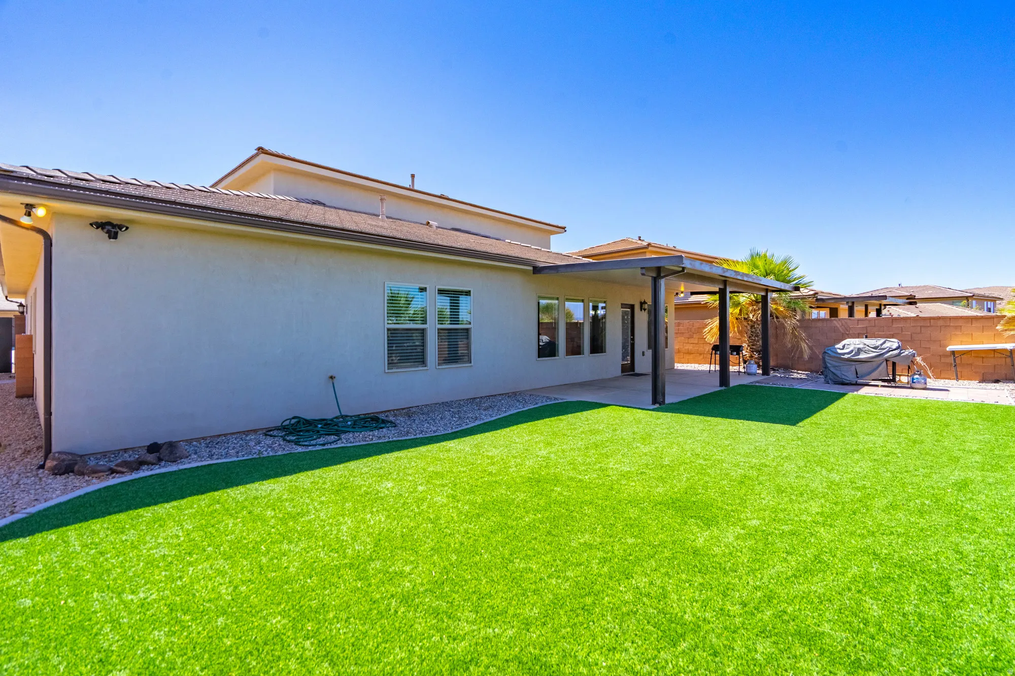 Expansive rear yard featuring artificial turf, a paved patio, and a covered patio area with a pergola