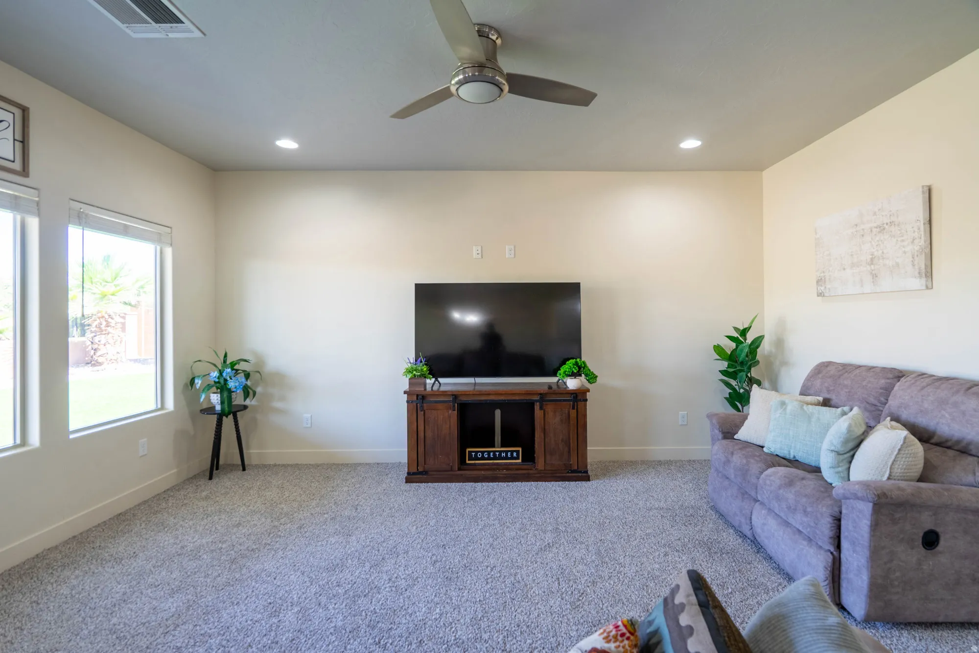 Spacious living area featuring light-toned walls, recessed lighting, and a ceiling fan with integrated lighting