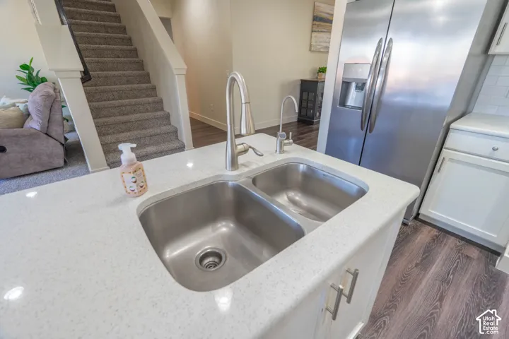 Kitchen island featuring a double basin stainless steel sink with a gooseneck faucet, white speckled countertop, and white cabinetry with silver hardware
