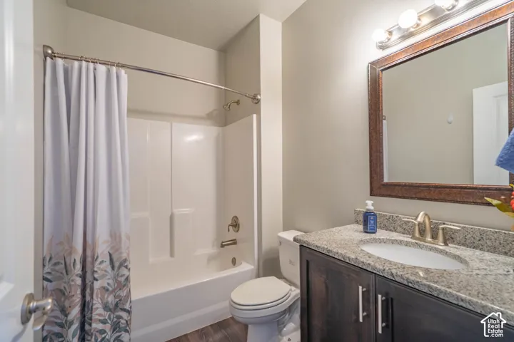 Bathroom featuring a full tub/shower combination, dark wood-finish vanity with granite-style countertop, undermount sink, and a framed mirror with vanity lighting
