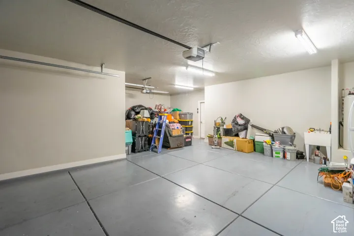 Expansive garage featuring gray finished concrete flooring, a utility sink, multiple fluorescent light fixtures, and a white interior door