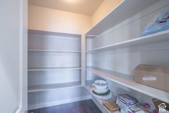 Walk-in pantry featuring extensive built-in shelving, durable wood-finish flooring, and bright overhead lighting