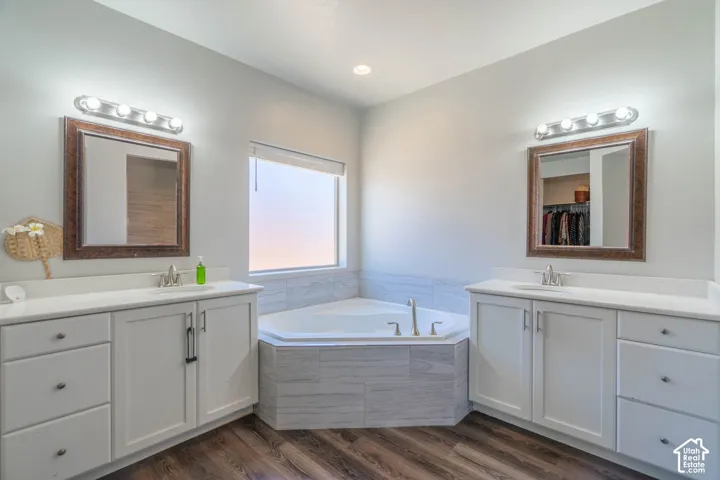 Bathroom featuring a corner soaking tub with tile surround, dual vanities with white cabinetry, integrated sinks, and individual mirrors with vanity lighting