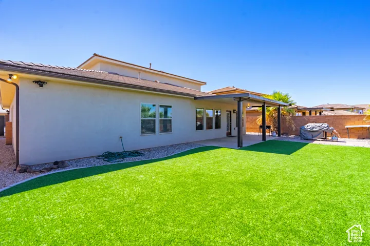 Expansive rear yard featuring artificial turf, a paved patio, and a covered patio area with a pergola