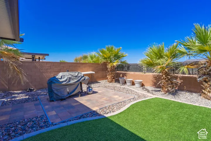 Backyard featuring artificial turf, a paver patio, a perimeter block wall, decorative rock landscaping, and mature palm trees