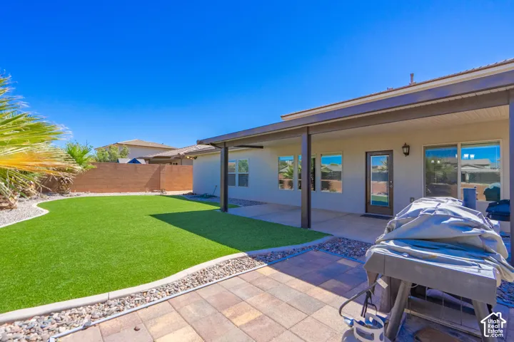 Private backyard featuring synthetic turf, decorative rock landscaping, a block wall perimeter, and a covered patio with a paver surface