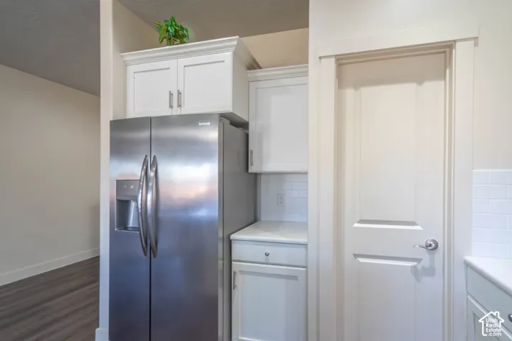 Stainless steel side-by-side refrigerator, white upper and lower cabinetry, white subway tile backsplash, and light-toned countertops