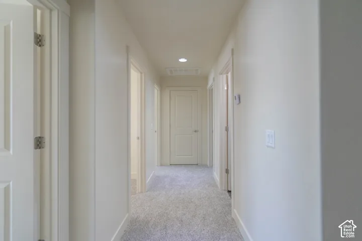 Hallway featuring light gray carpeting, white walls, recessed ceiling lighting, and multiple paneled doors