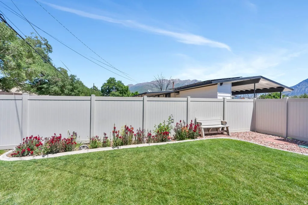 Expansive backyard featuring a green lawn, a light-colored privacy fence, and a planting bed with red blooming flowers